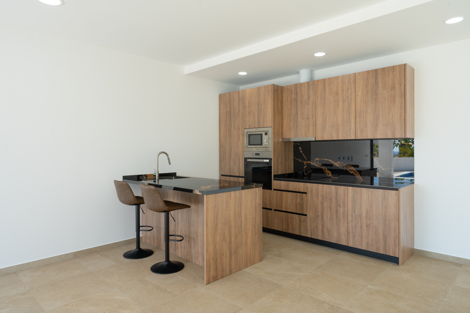 Designerküche mit Holzfronten, Arbeitsplatte aus schwarzem, gemasertem Stein und Kochinsel mit Barhockern. Ausgestattet mit Einbaugeräten und moderner Deckenbeleuchtung.