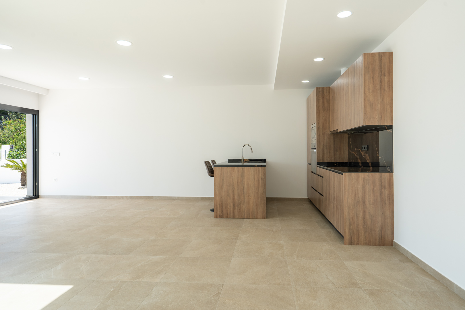 Designerküche mit Holzfronten, dunkler gemaserter Arbeitsplatte und Kochinsel in einem offenen Wohnbereich mit großformatigen Feinsteinzeugfliesen.