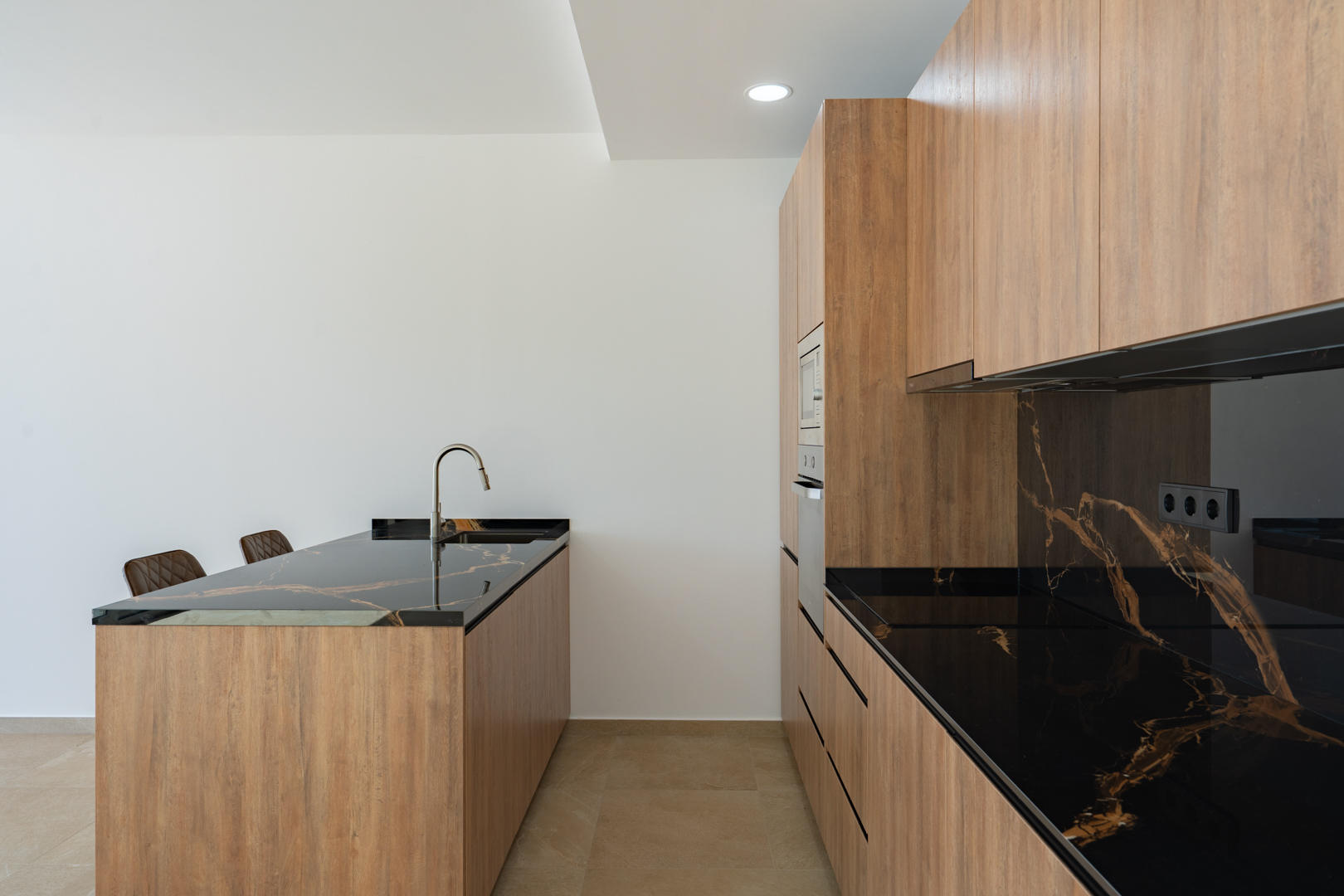 Designerküche mit Schränken in Holzoptik, dunklen, gemaserten Arbeitsplatten und einer Kochinsel mit integriertem Spülbecken und minimalistischer Armatur.