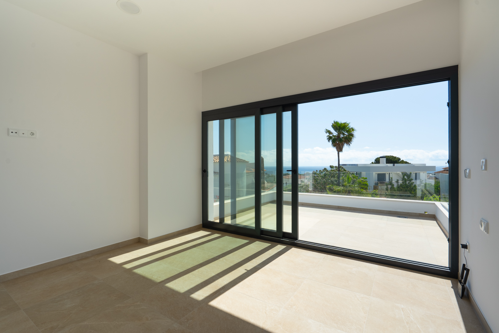 Heller Innenraum mit Feinsteinzeugböden und großen Glasschiebetüren, die auf eine private Terrasse mit weitem Blick auf das Mittelmeer führen.