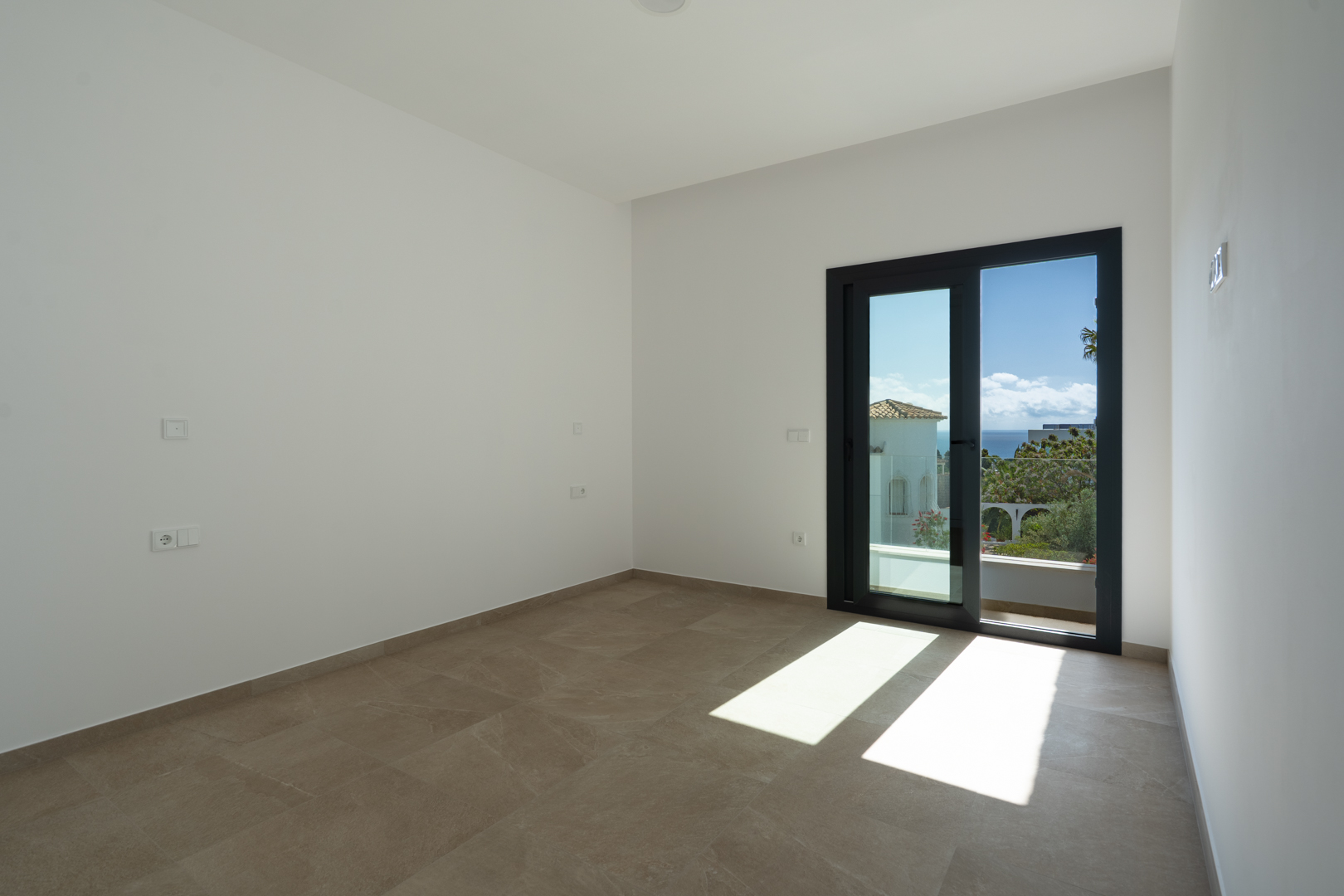 Helles Schlafzimmer mit großformatigen Feinsteinzeugfliesen und direktem Zugang zu einer privaten Terrasse mit weitem Blick auf das Mittelmeer.