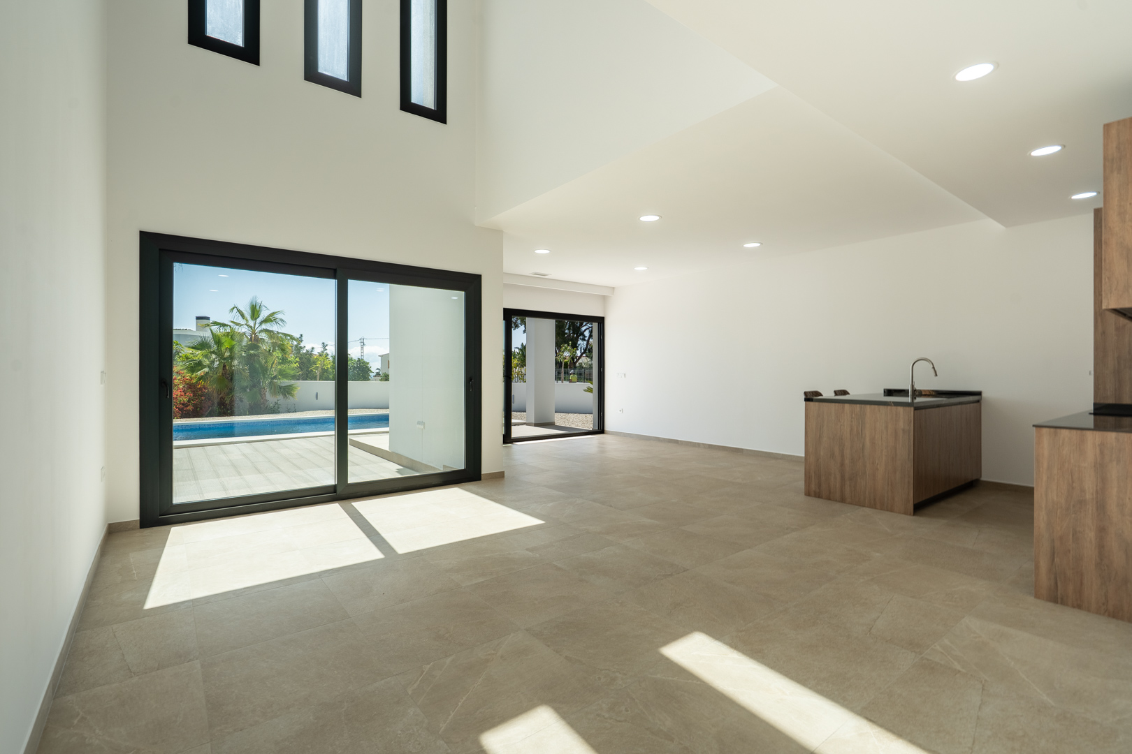 Lichtdurchfluteter, doppelt hoher Wohnbereich mit offener Designerküche, Feinsteinzeugböden und direktem Zugang zur Poolterrasse durch Glasschiebetüren.