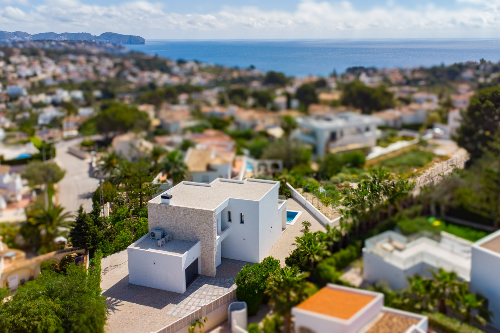 Luftaufnahme der modernen Villa mit Natursteinfassade und weißer Architektur, gelegen in einem Wohngebiet mit weitem Blick auf das Mittelmeer.