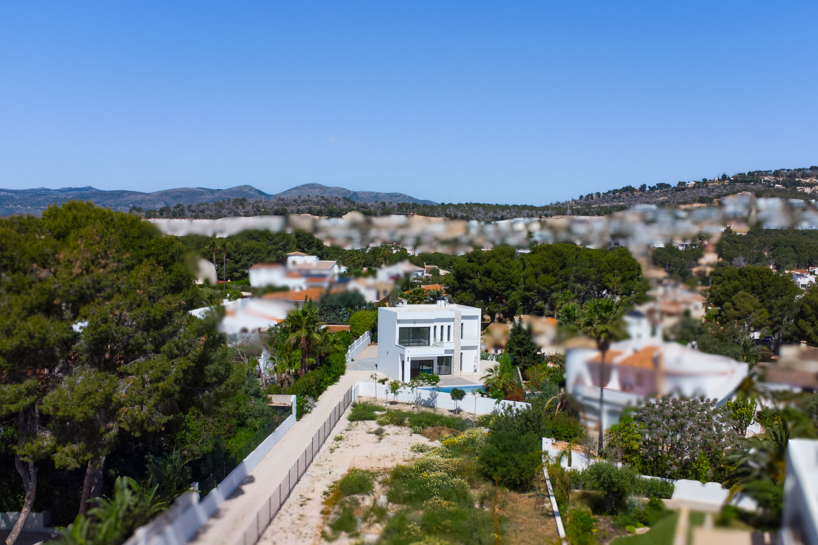 Luftaufnahme der modernen weißen Villa auf einem weitläufigen, flachen Grundstück, umgeben von Pinien und mit Blick auf die umliegenden Berge.