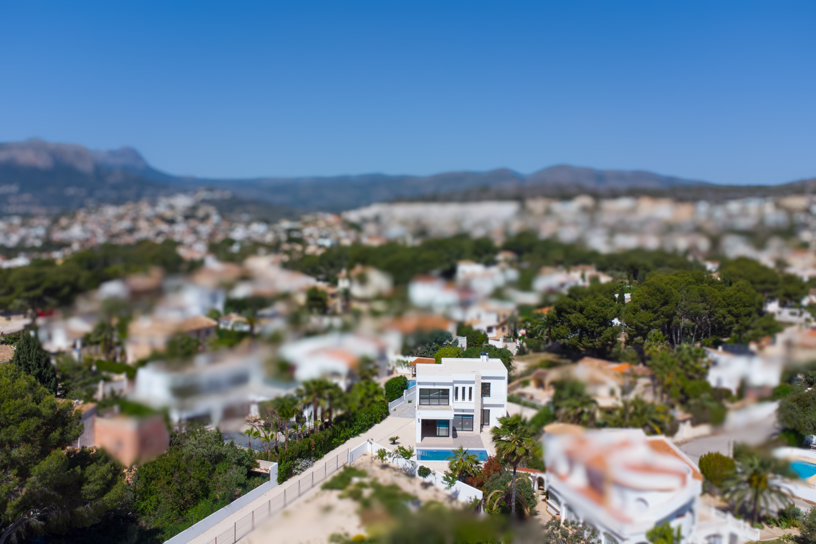 Luftaufnahme der modernen zweistöckigen Villa mit weißer Fassade und Pool, die ihre Lage inmitten der mediterranen Landschaft von Benissa verdeutlicht.