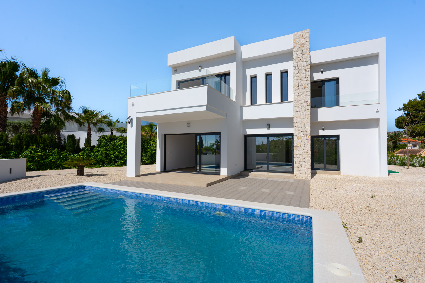 Moderne zweistöckige Villa mit Natursteinwand, privatem Pool und Glasgeländer-Terrassen in einem pflegeleichten Garten mit Palmen.