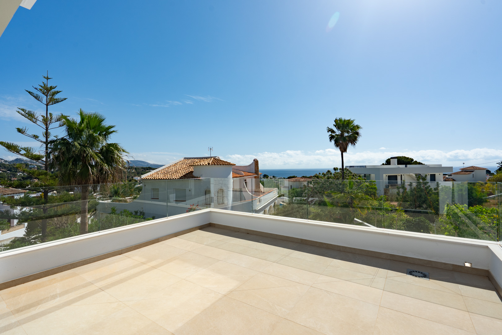 Obere Terrasse mit großformatigen Feinsteinzeugfliesen und Glasgeländern, die einen weiten Blick auf das Mittelmeer und die umliegende Wohngegend von Benissa bieten.