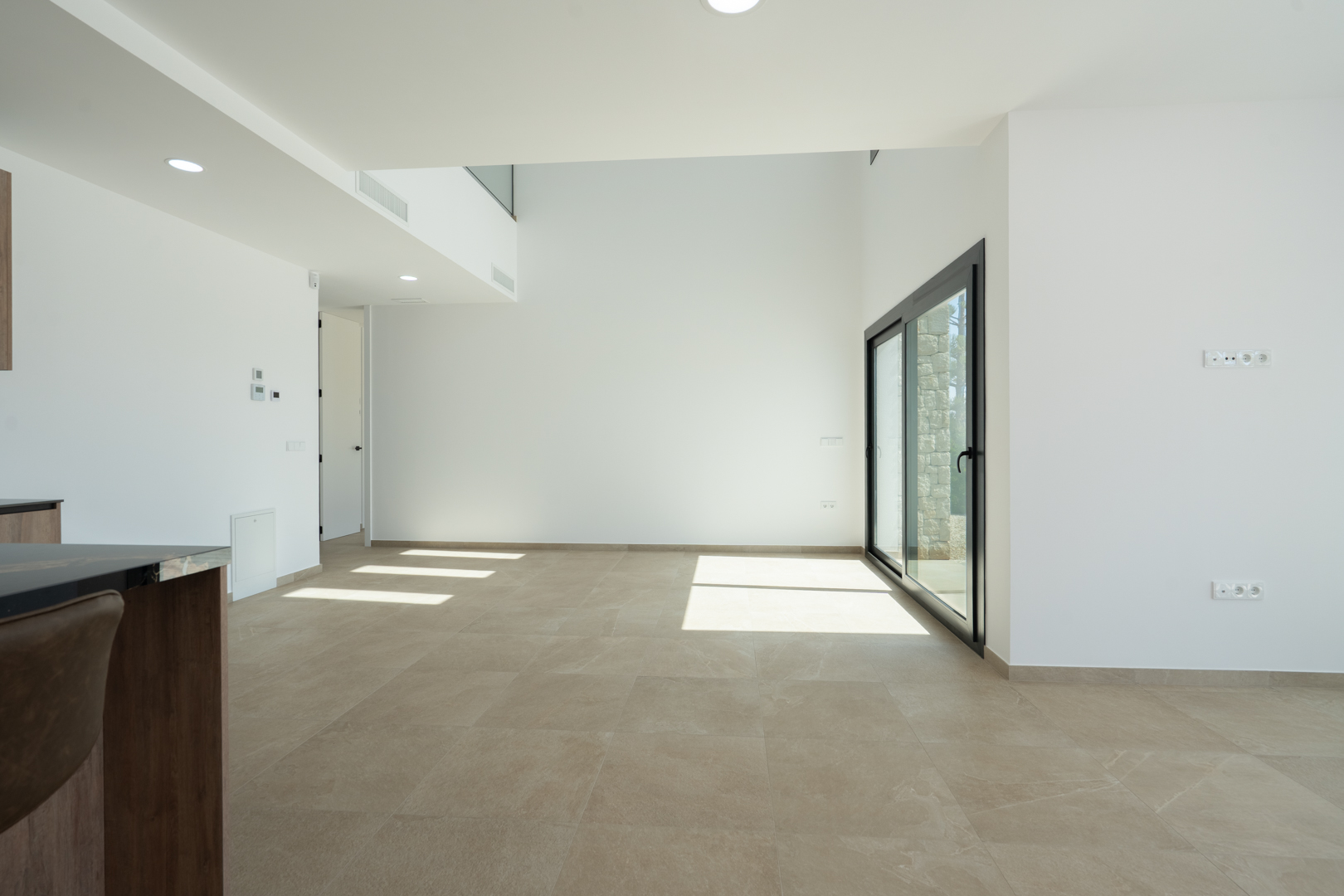 Offener Wohn-Essbereich mit doppelter Deckenhöhe, großformatigen Feinsteinzeugfliesen und bodentiefen Glasschiebetüren für optimalen Lichteinfall.