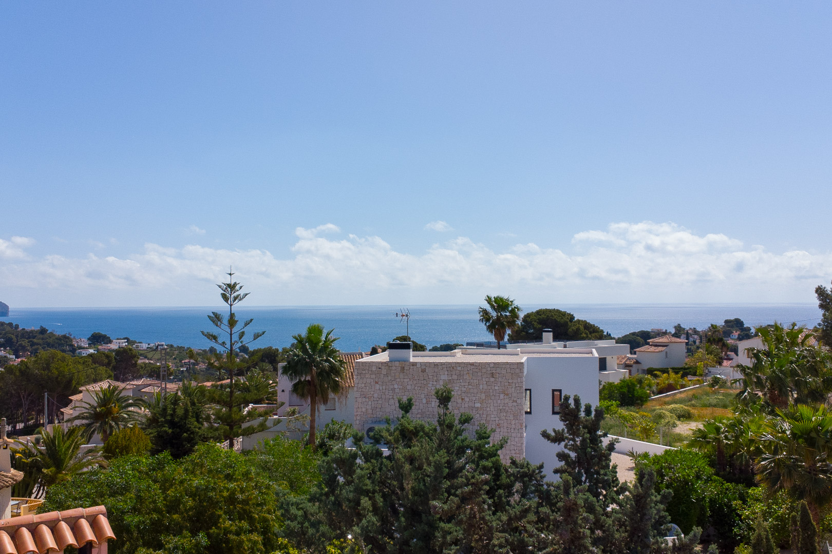 Panoramablick vom Grundstück auf das Mittelmeer, mit weißer Villenarchitektur und üppiger mediterraner Vegetation unter strahlend blauem Himmel.