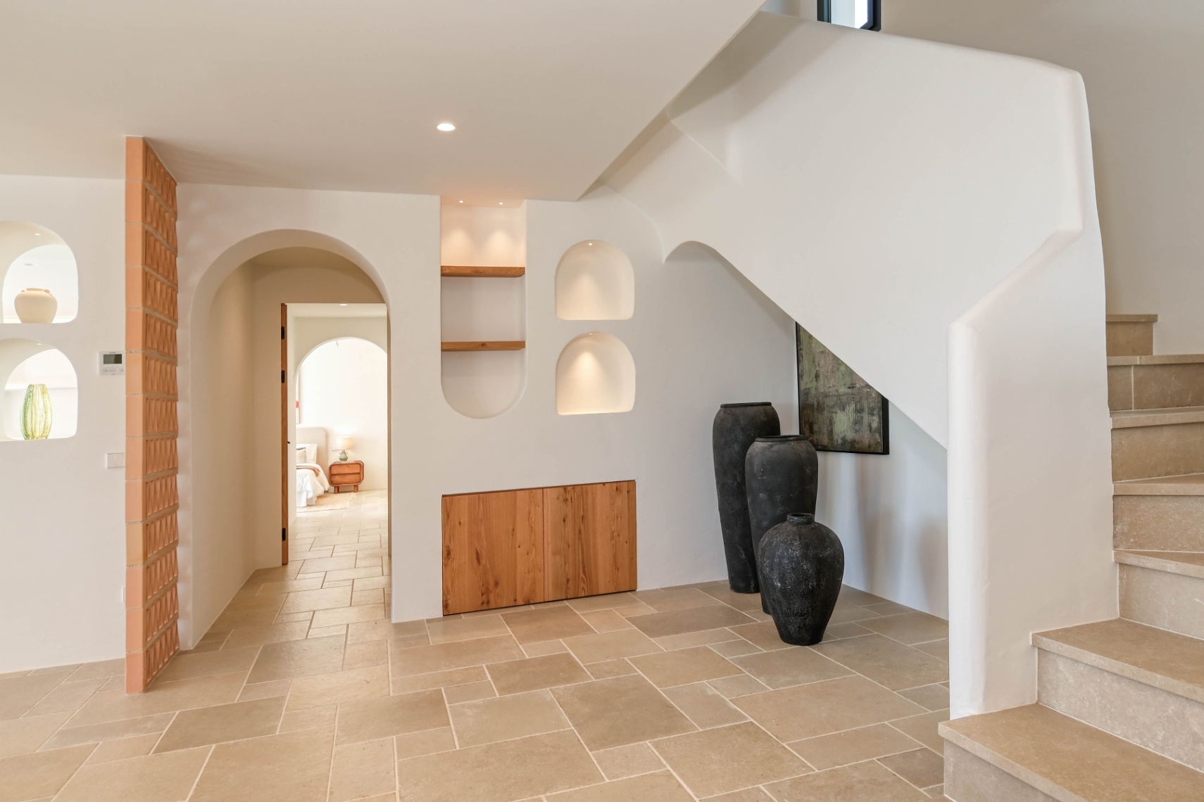 Flur im mediterranen Stil mit Steintreppe, beleuchteten Wandnischen und integrierten Holzschränken. Natursteinböden führen durch elegante Rundbögen in die Räume.