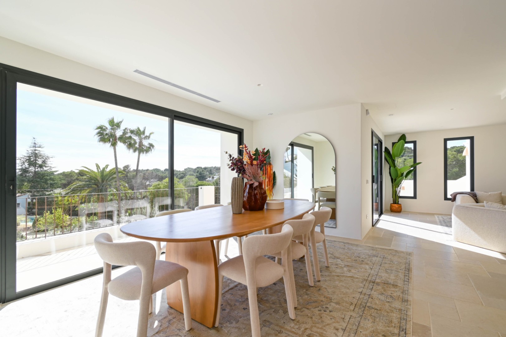 Heller Essbereich mit ovalem Holztisch und großen Glasschiebetüren, die einen weiten Blick auf Palmen und die mediterrane Landschaft bieten.