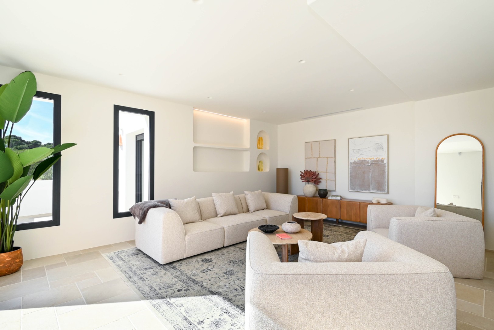 Heller Wohnbereich mit modularen Sofas in Beigetönen, integrierten Wandnischen mit LED-Beleuchtung und Natursteinboden, der für ein elegantes Ambiente sorgt.