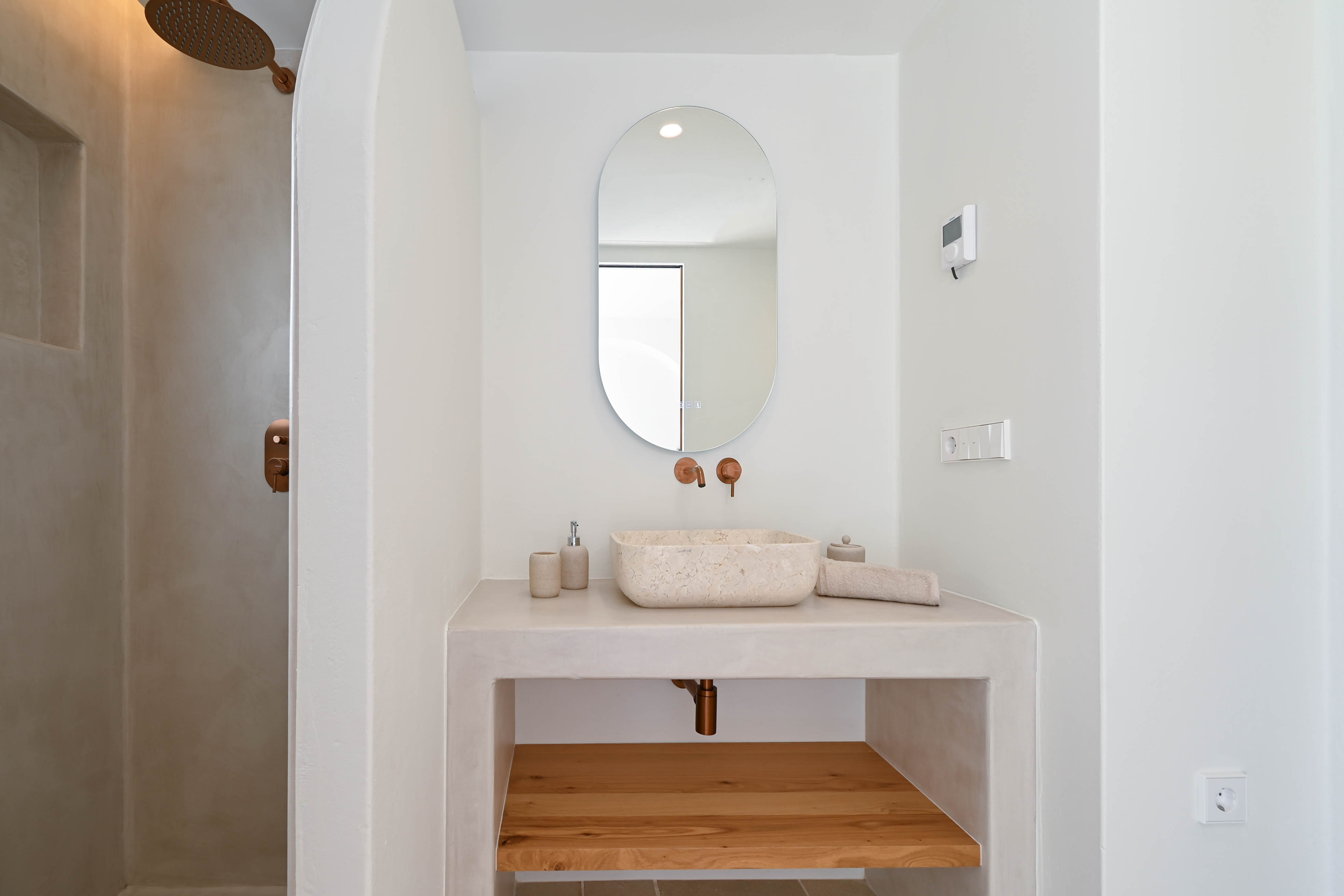 Modernes Badezimmer mit Mikrozement-Oberflächen, Natursteinwaschbecken und kupferfarbenen Armaturen. Ein integrierter Waschtisch mit Holzregal und begehbarer Dusche.