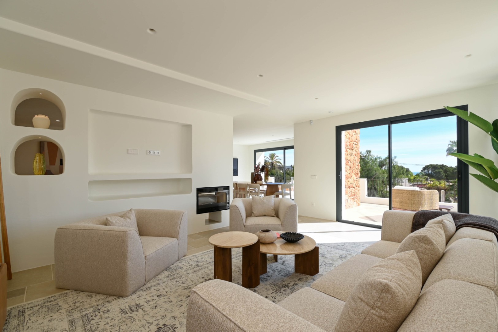 Modernes Wohnzimmer mit integriertem Kamin, minimalistischen Wandnischen und großen Glasschiebetüren, die den Innenraum mit der Terrasse verbinden.
