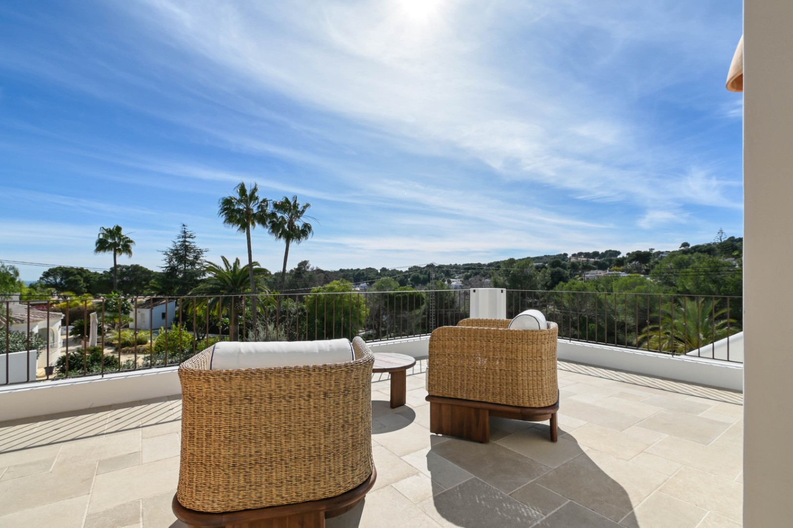Obere Terrasse mit Natursteinboden und Korbsesseln, die einen weiten Blick auf die mediterrane Hügellandschaft und Palmen von Moraira bietet.