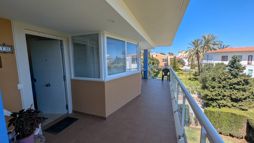 Eingangsterrasse mit Fliesenboden und Glasbalustrade, die einen Blick auf die gemeinschaftlichen Grünflächen und benachbarten mediterranen Villen bietet.