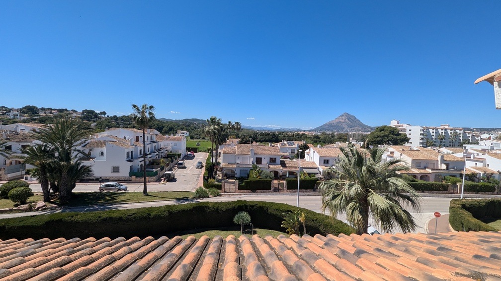 Erhöhter Blick von der Terrasse über die Terrakotta-Dachziegel auf das Wohnviertel von Jávea und den markanten Berg Montgó unter strahlend blauem Himmel.