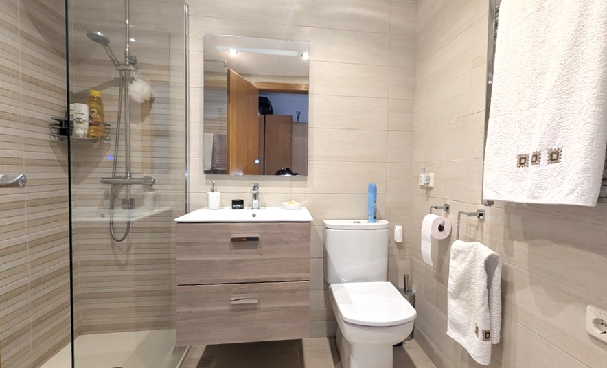 Modernes Badezimmer mit Glasduschkabine, schwebendem Waschtisch in heller Holzoptik und horizontal gestreiften Wandfliesen in Beigetönen.