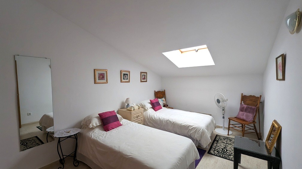 Schlafzimmer im Dachgeschoss mit zwei Einzelbetten, einem Dachfenster für Tageslicht und hellen Fliesenböden.