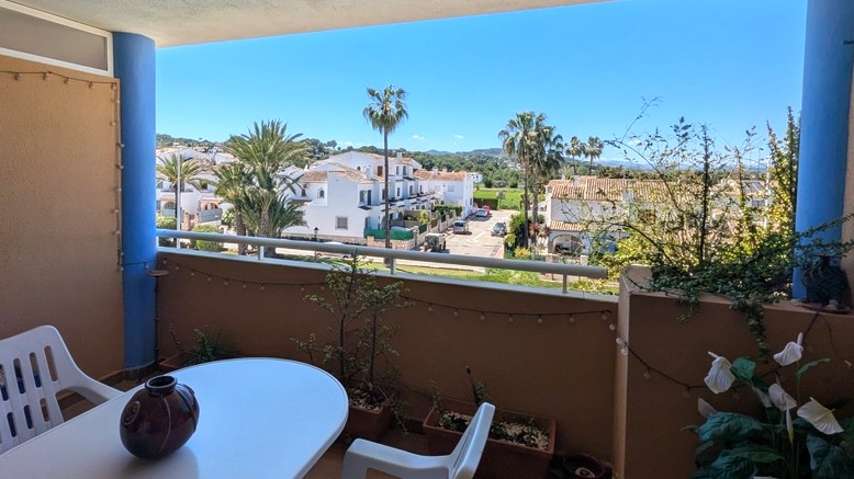 Überdachte Terrasse mit Essbereich und freiem Ausblick auf mediterrane Villen, Palmen und das Montgó-Massiv in der Ferne.