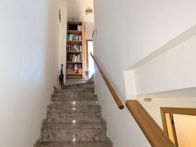 Die elegante Innentreppe verfügt über polierte Marmorstufen mit integrierter Beleuchtung und einem warmen Holzgeländer, die zum Obergeschoss mit Bücherregal führt.