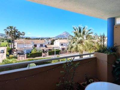Offene Terrasse mit weißem Geländer und Topfpflanzen, mit weitem Blick über Wohngebiete, Grünflächen und den markanten Berg Montgó unter klarem Himmel.
