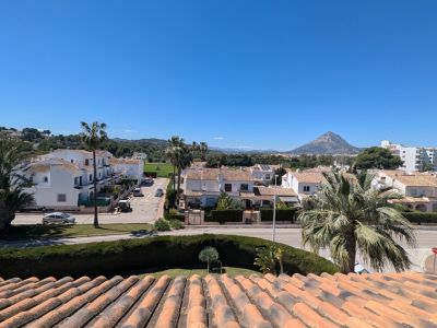 Panoramablick von der Terrasse mit Terrakottadächern, Wohnstraßen, üppigen Palmen und dem majestätischen Montgó-Berg unter klarem blauem Himmel.