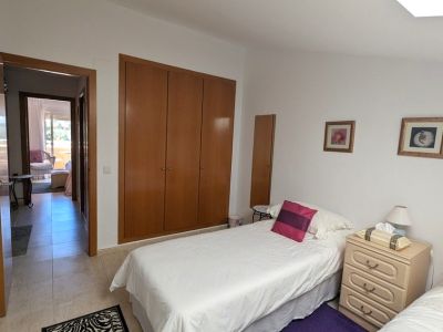 Schlafzimmer mit zwei Einzelbetten, einem Einbauschrank aus Holz und Nachttisch. Eine offene Tür bietet einen Blick auf eine Außenterrasse.