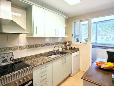 Voll ausgestattete Küche mit hellen Schränken, Granit-Arbeitsplatten, integriertem Kochfeld und Backofen sowie einem Fenster zum angrenzenden Hauswirtschaftsraum.