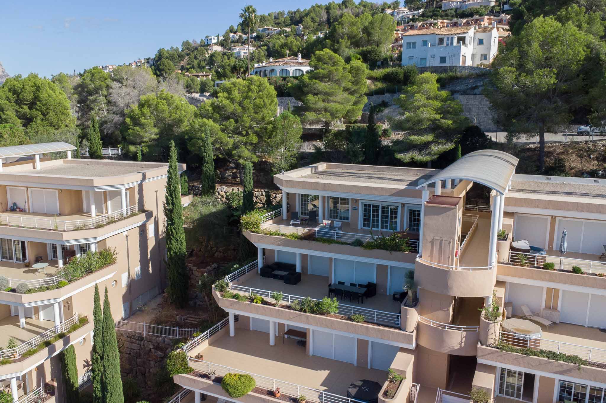 Außenansicht der Anlage Las Mimosas mit terrassenförmiger Architektur, weitläufigen privaten Balkonen und erdfarbenen Fassaden, eingebettet in die bewaldeten Hänge von La Sella.