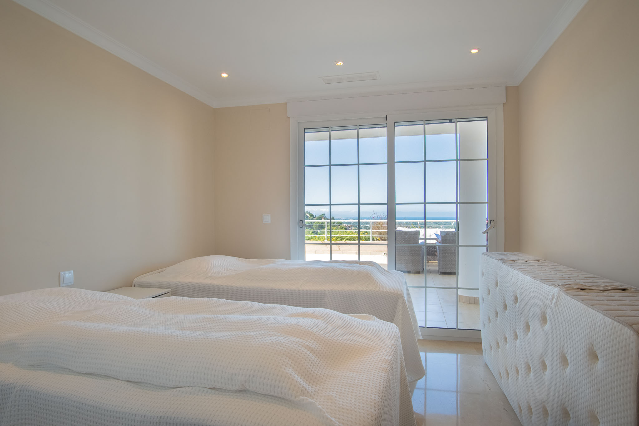 Doppelzimmer mit Marmorboden und direktem Zugang zur Terrasse durch Sprossenfenster, die einen weiten Blick auf das Meer bieten.