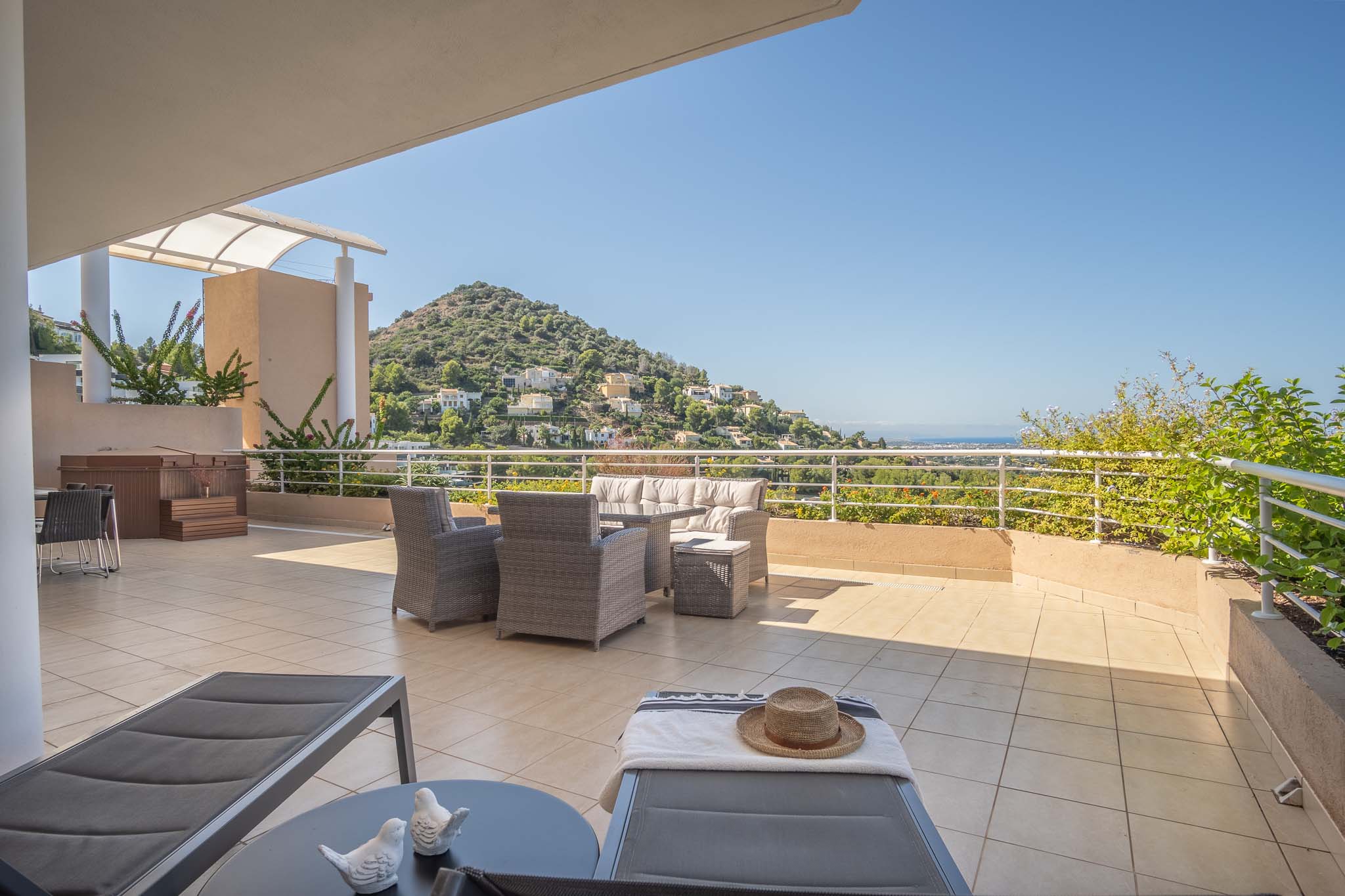 Großzügige Fliesenterrasse mit grauen Korbmöbeln, privatem Whirlpool und Sonnenliegen. Sie bietet einen Panoramablick auf die umliegenden Hügel und das Mittelmeer.