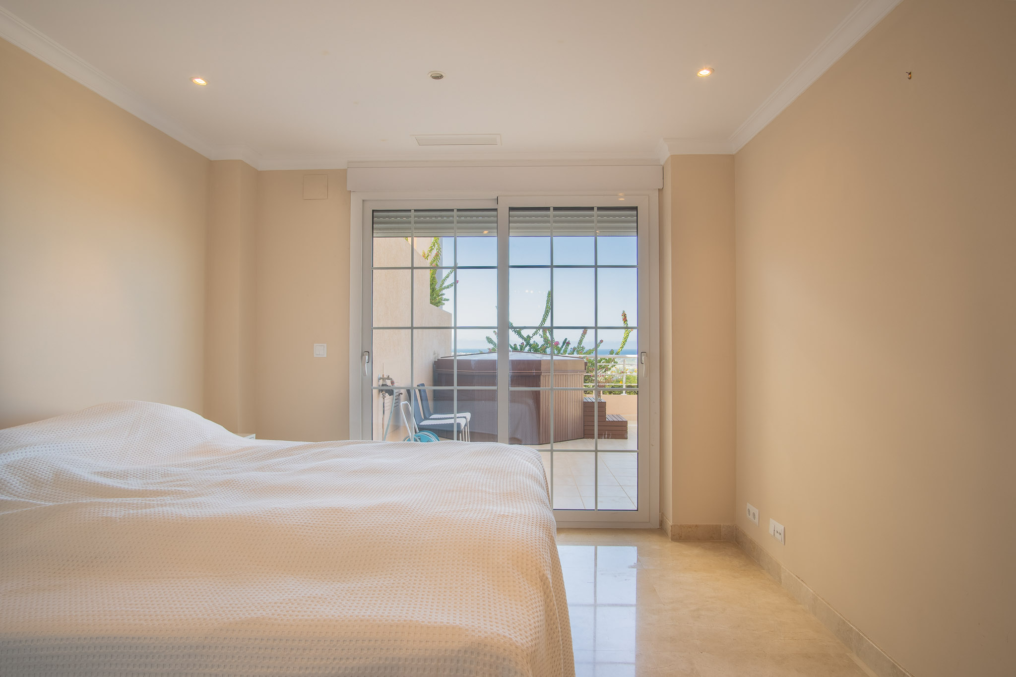 Helles Schlafzimmer mit Marmorboden und direktem Zugang zur privaten Terrasse mit Whirlpool und Meerblick.