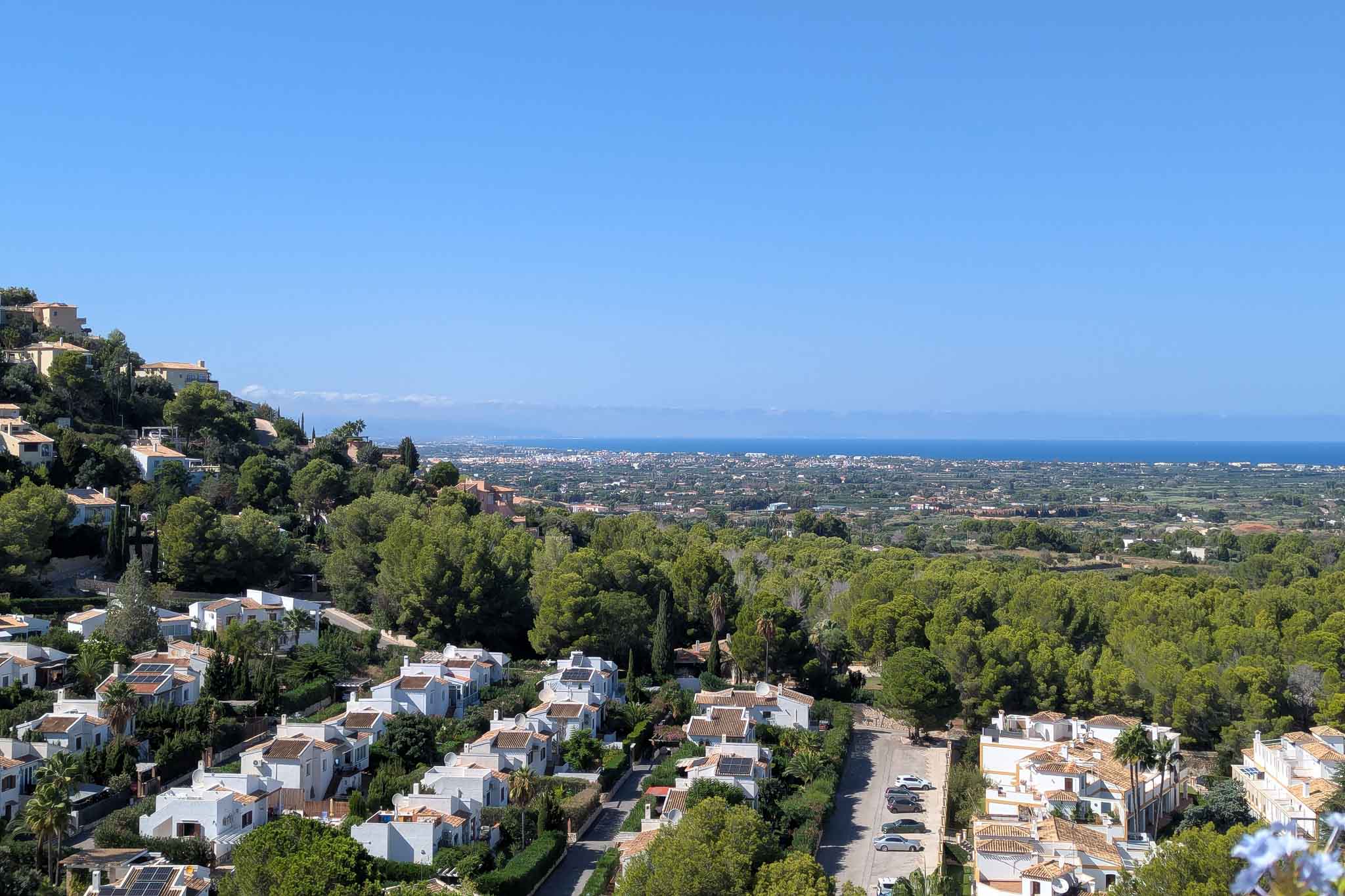 Panoramablick von La Sella auf die Küste von Dénia mit weißen Villen inmitten von Pinienwäldern und dem weiten Mittelmeer unter klarem blauem Himmel.