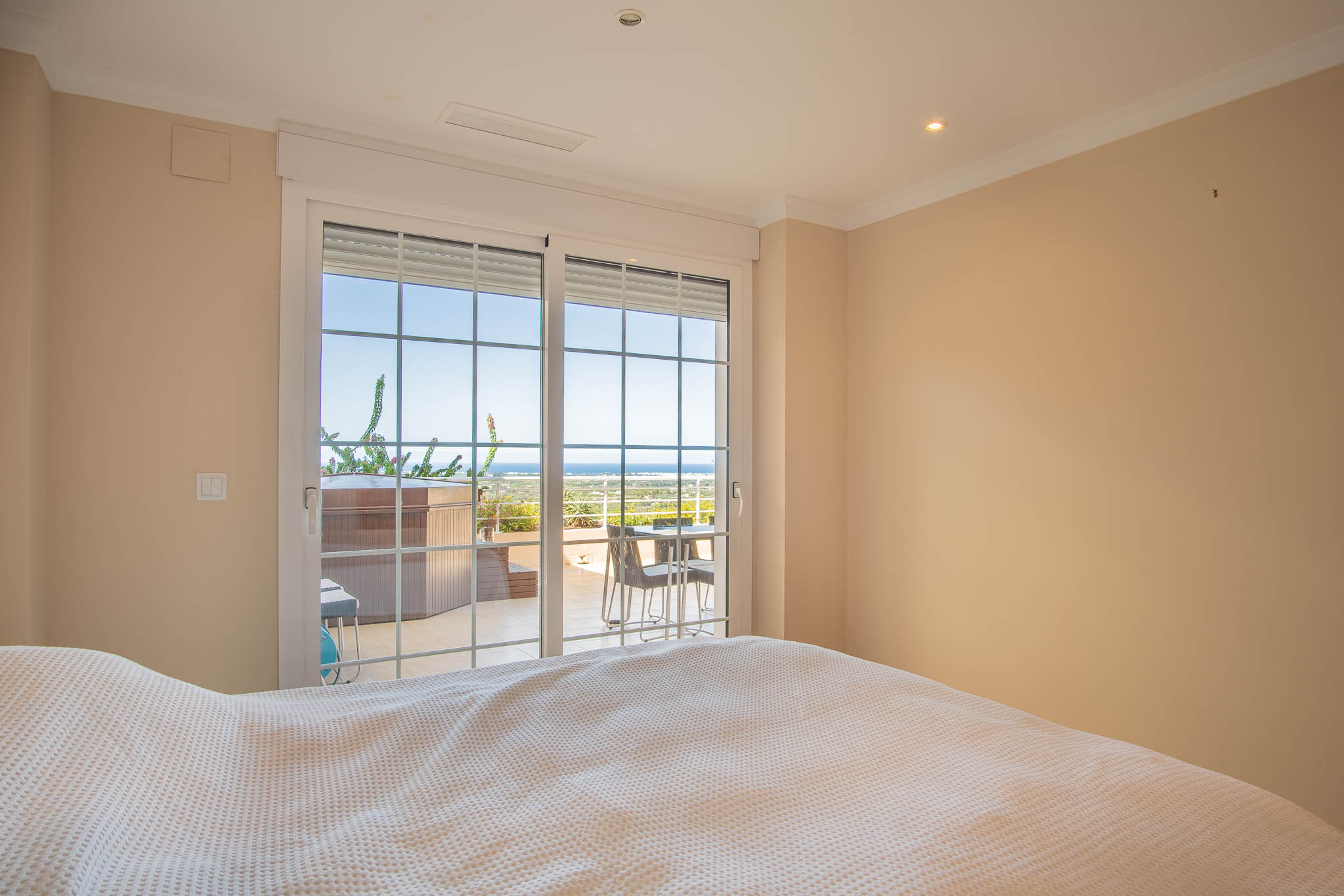 Schlafzimmer mit direktem Terrassenzugang durch großzügige Fenstertüren. Der Außenbereich umfasst einen privaten Whirlpool und weiten Blick auf das Mittelmeer.