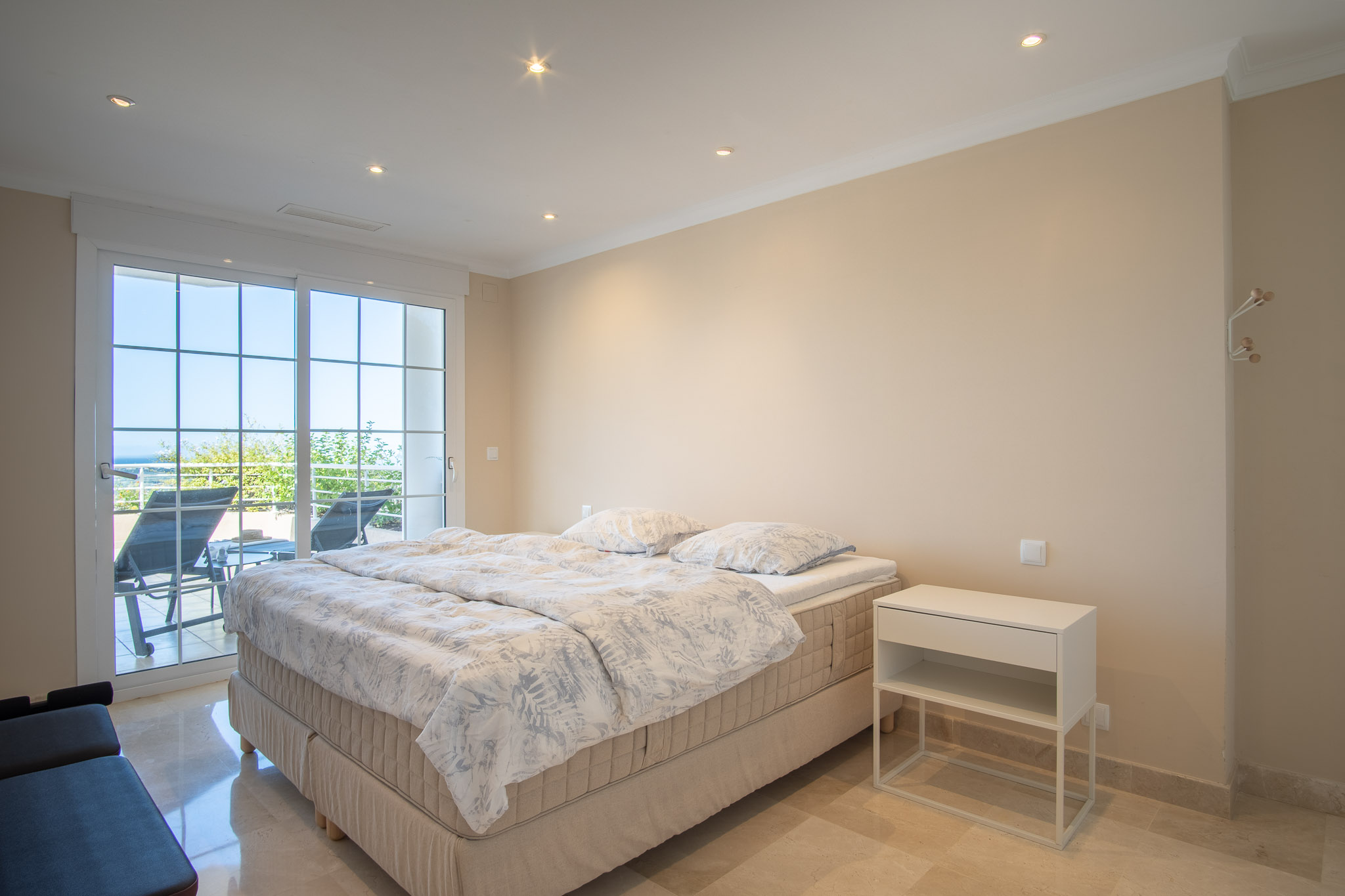 Schlafzimmer mit Marmorboden und Einbaustrahlern. Große Glasschiebetüren führen direkt auf die Terrasse mit Blick auf die gepflegten Außenanlagen und das Meer.