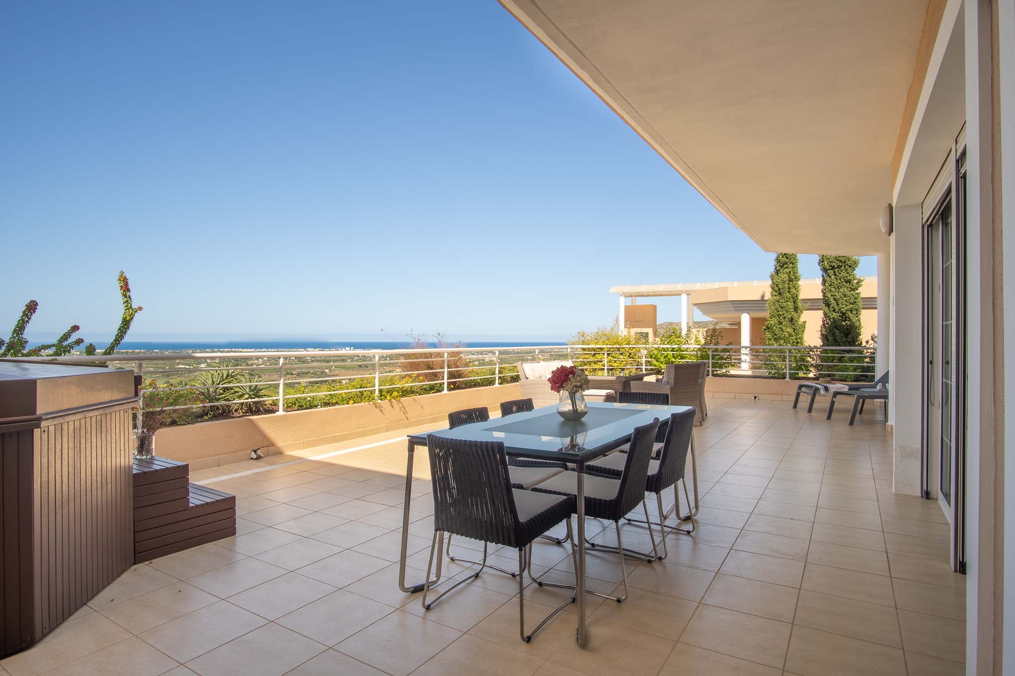 Weitläufige Terrasse mit privatem Whirlpool, Essbereich im Freien und Panoramablick auf das Mittelmeer. Der Boden ist mit Keramikfliesen und einem weißen Geländer ausgestattet.