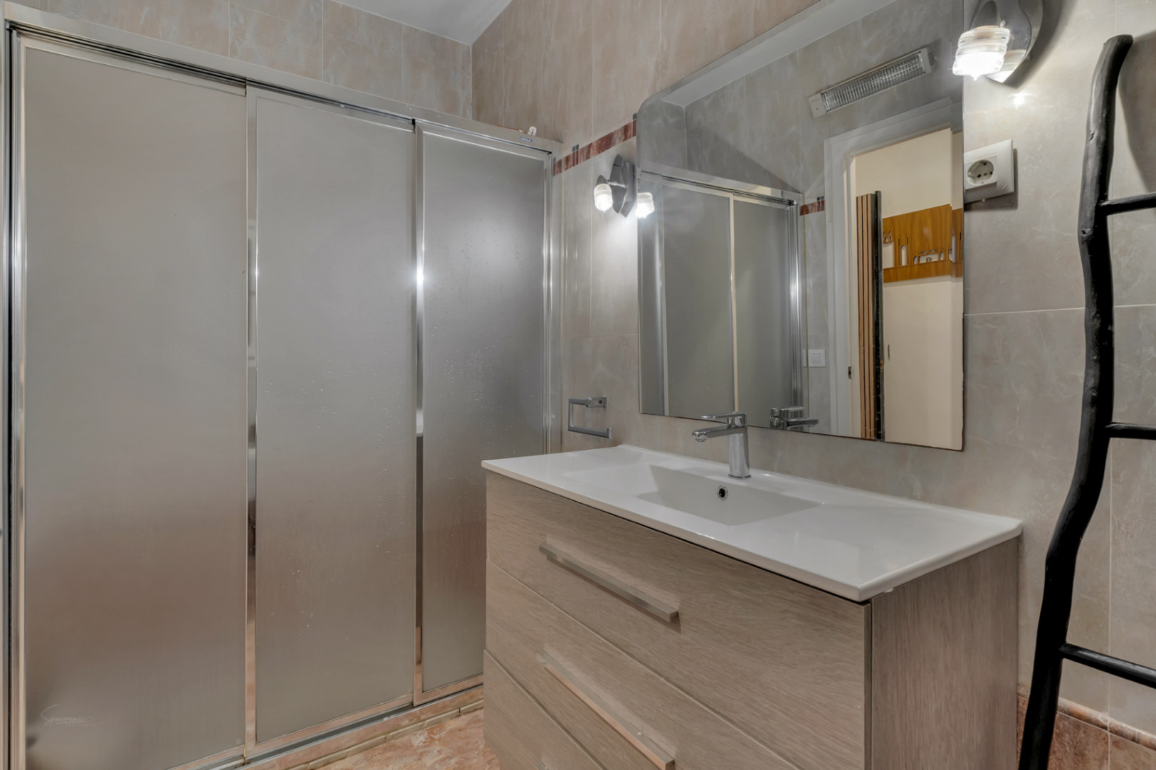 Badezimmerdetail mit eingelassenem Waschbecken in hellem Holzunterschrank und Dusche mit Schiebetüren.