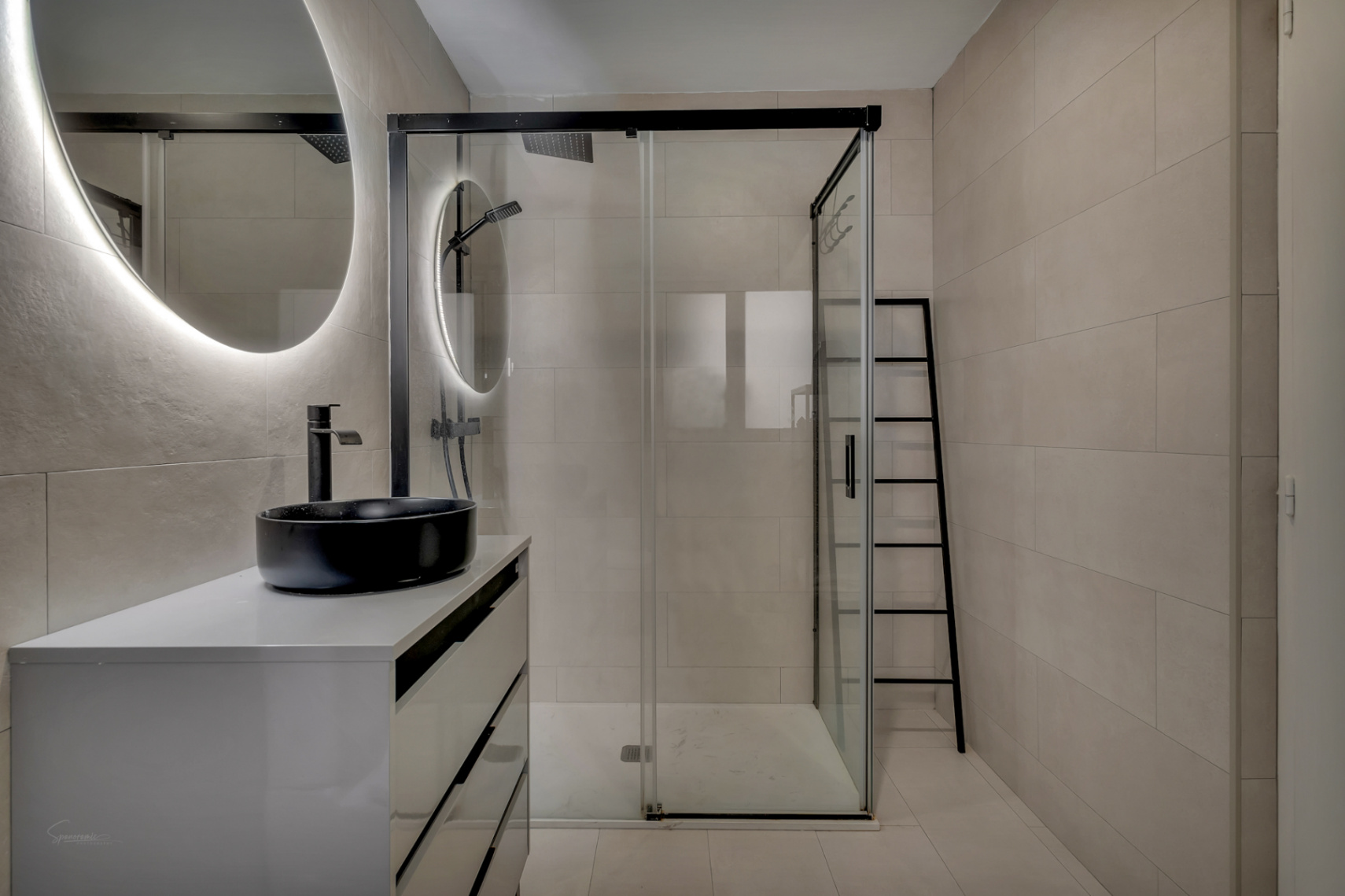 Detail des modernen Badezimmers mit schwarzem Aufsatzwaschbecken auf weißer Arbeitsplatte und Glasdusche.