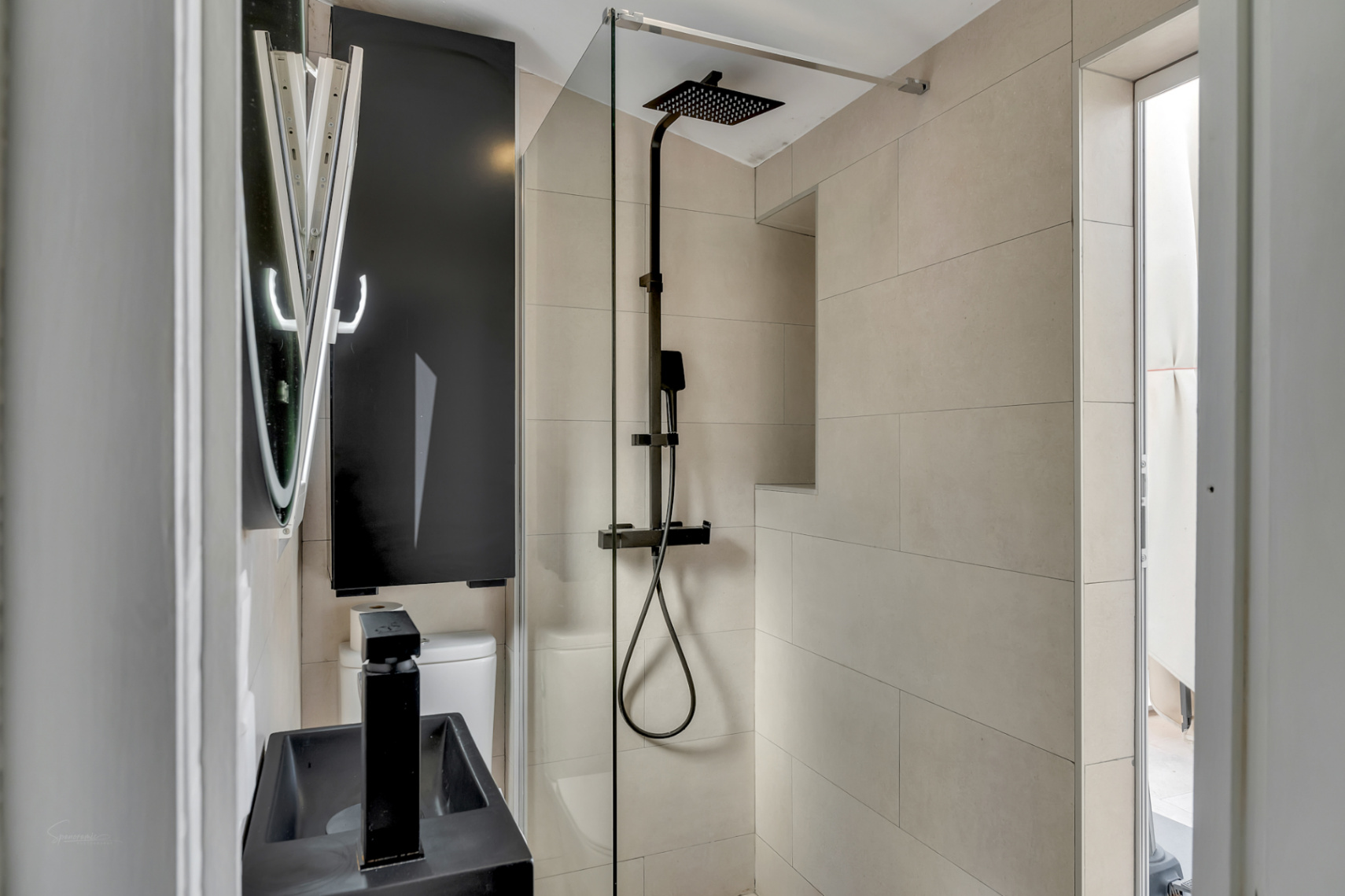 Detail des modernen Badezimmers mit schwarzer Regendusche, schwarzem Waschbecken und cremefarbenen Fliesen.