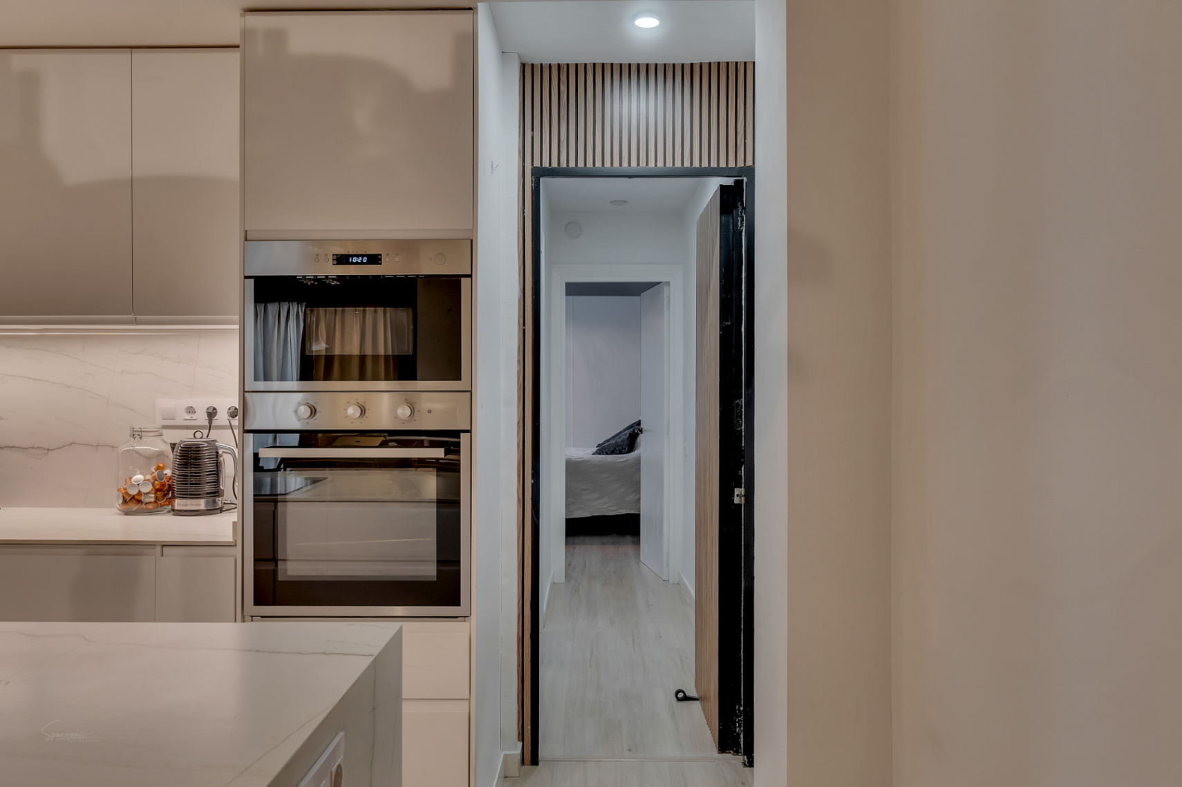 Küchendetail mit Einbaubackofen und Blick auf das Schlafzimmer durch eine Tür mit Holzdesign.