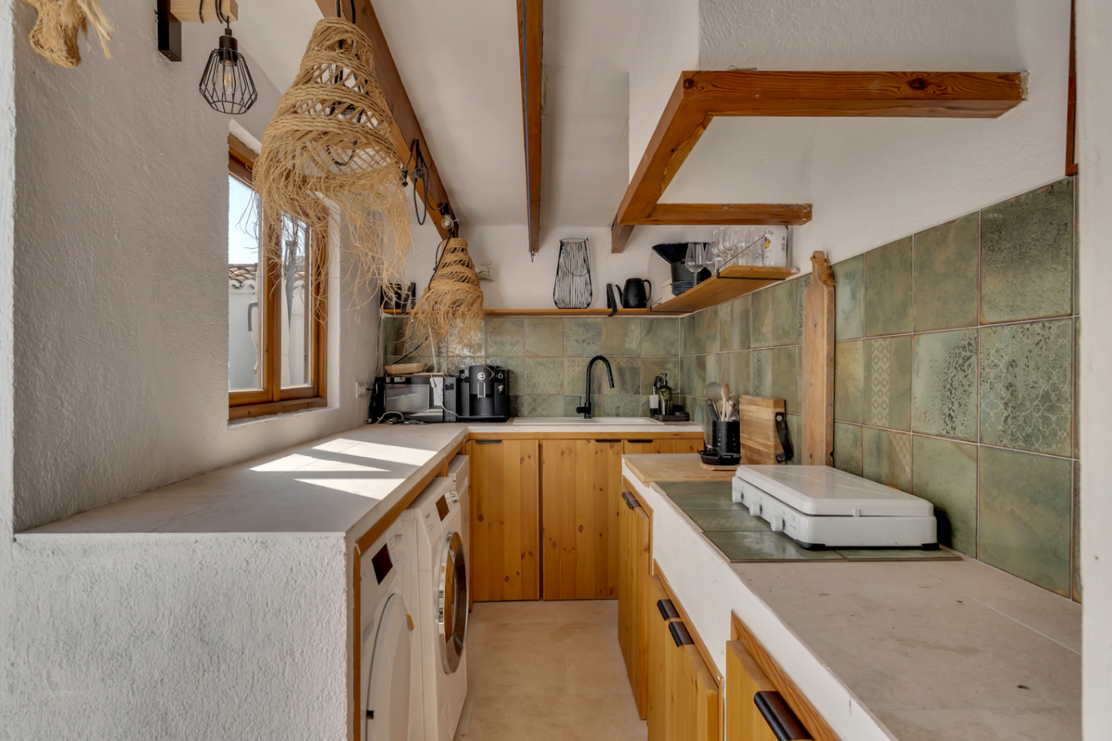 Küchendetail mit hellen Holzschränken, eingebauter Arbeitsplatte und grünem Fliesenspiegel.