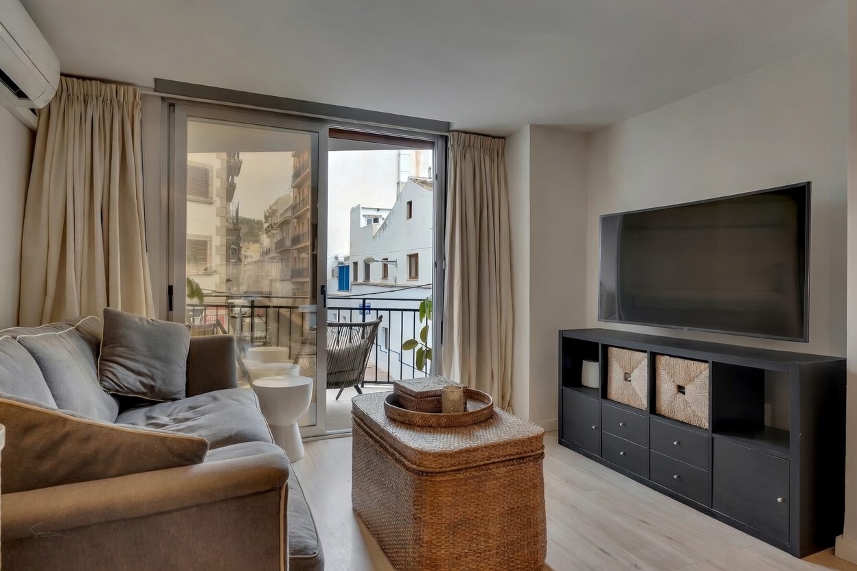 Modernes Wohnzimmer mit grauem Sofa, schwarzem TV-Schrank und Zugang zum Balkon mit Stadtblick.