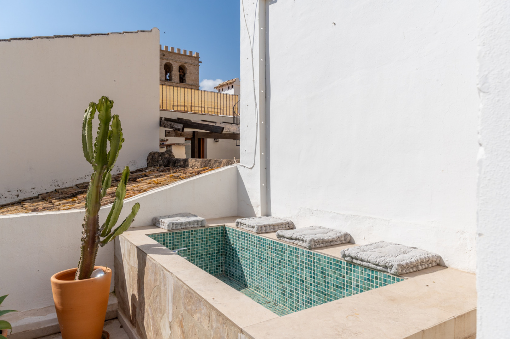 Terrassendetail mit türkisfarbenem Mosaik-Jacuzzi und Topf-Kaktus mit Blick auf die Altstadt.