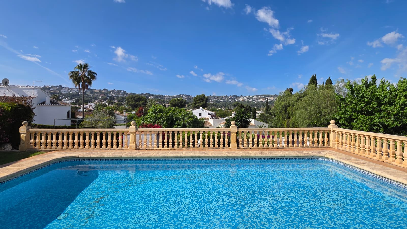 Außenpool mit blauen Mosaikfliesen und klassischer Steinbalustrade mit weitem Blick über die umliegenden Hügel und Wohngebiete von Jávea.
