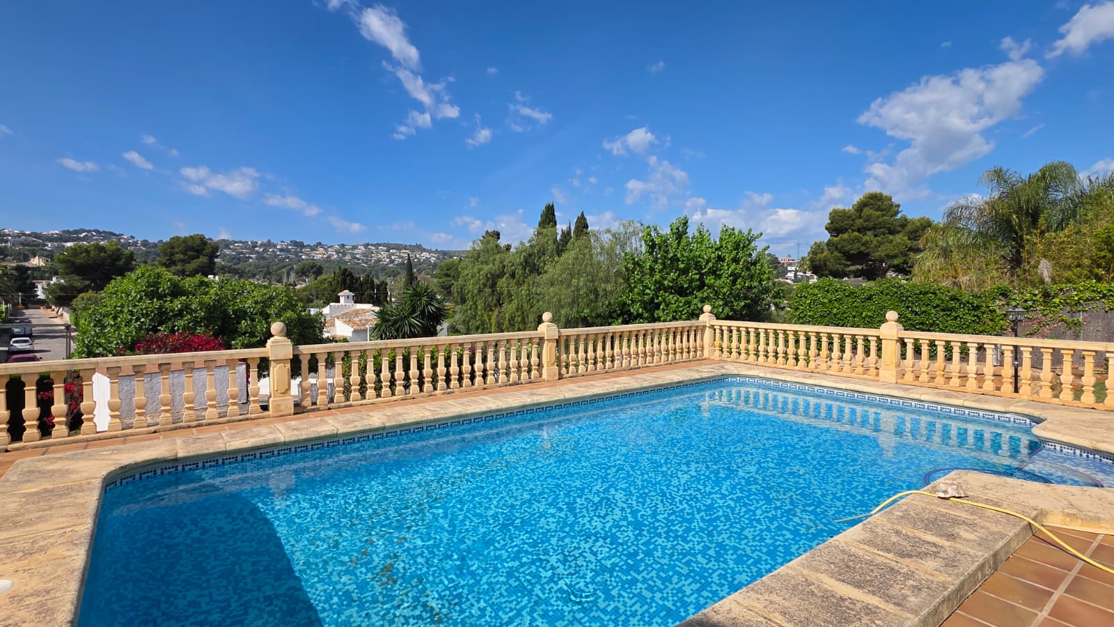 Erhöhter Pool mit blauem Mosaik, umgeben von einer klassischen Steinbalustrade mit weitem Blick über die Hügellandschaft von Jávea.