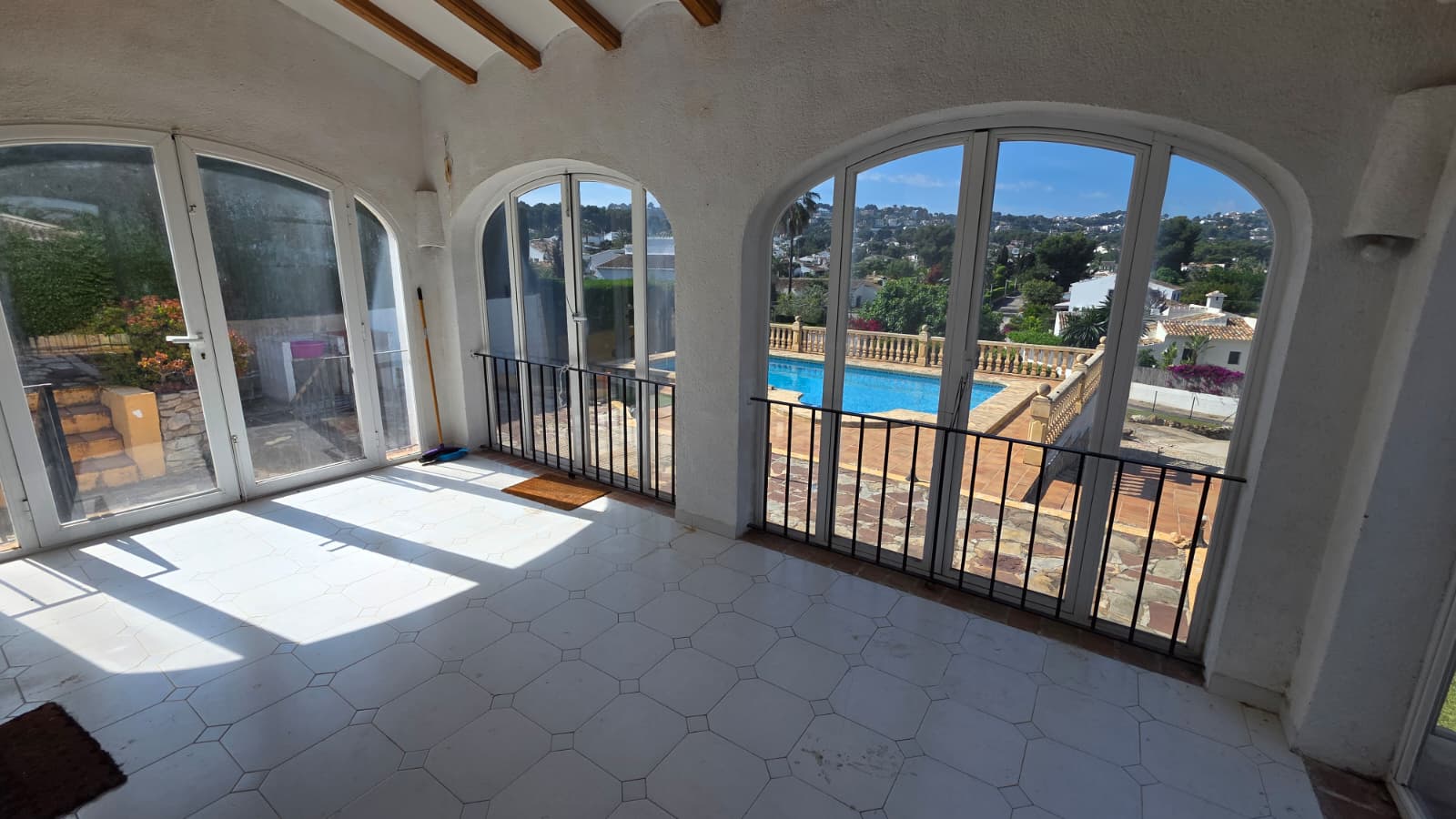 Verglaste Naya mit Rundbogenfenstern, weißen Fliesen und Holzbalken, mit Blick auf den privaten Pool und die hügelige Landschaft von Jávea.
