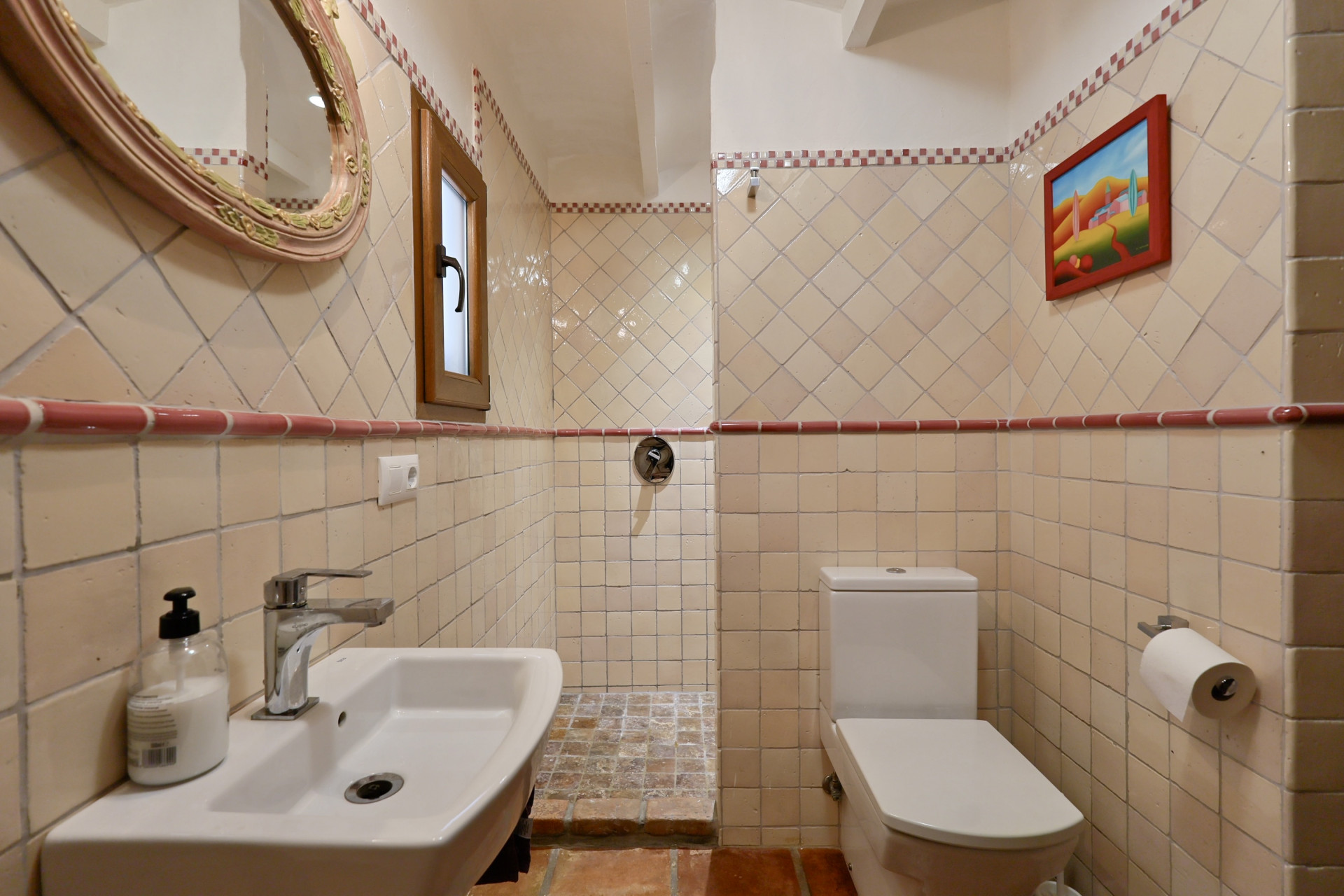 Badezimmerdetail mit cremefarbenen Fliesen, ovalem Spiegel und weißem Waschbecken in Villa in Jávea.