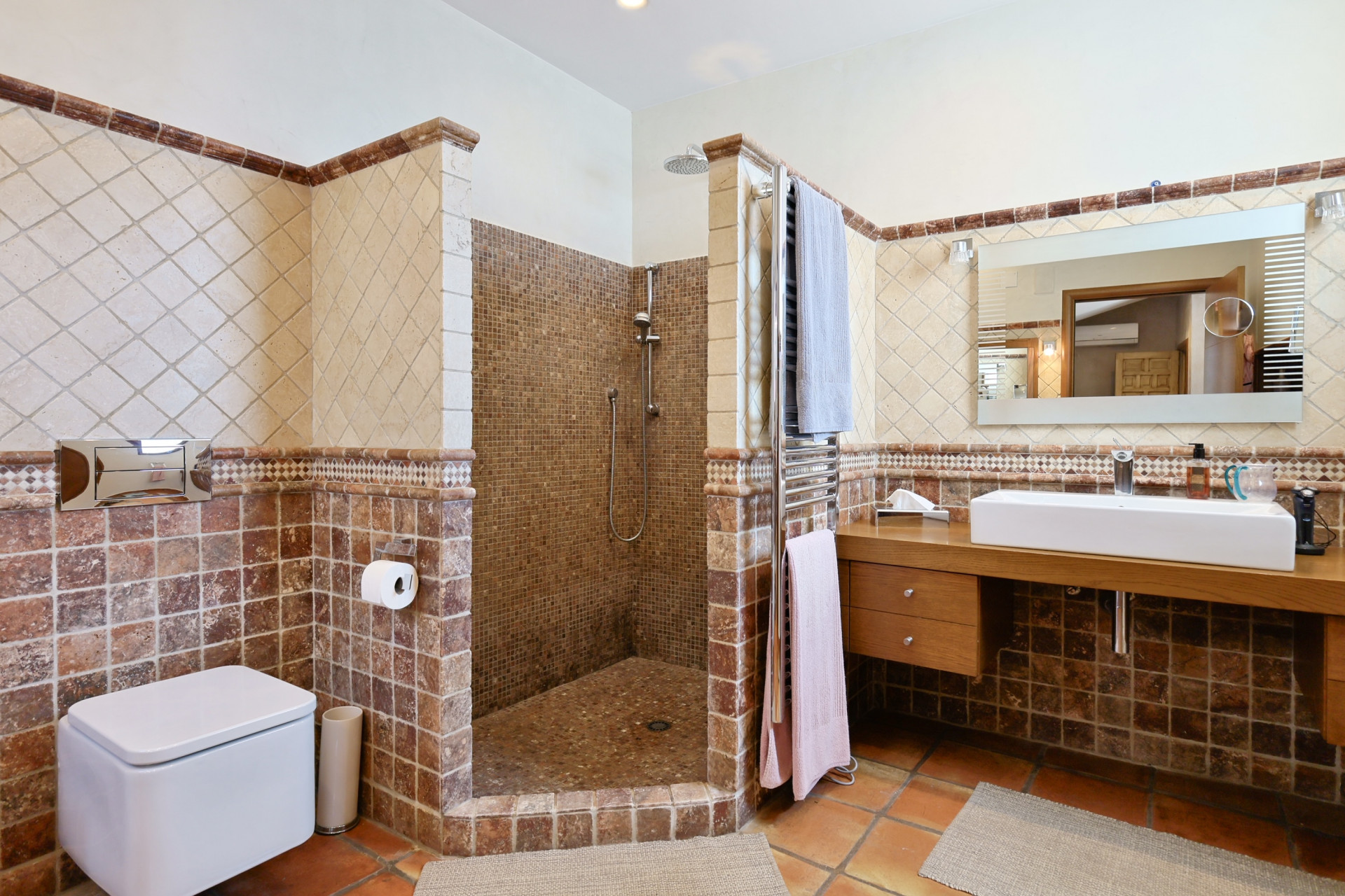 Badezimmerdetail mit Mosaikdusche, modernem Waschbecken auf Holzarbeitsplatte und rustikalen Fliesen.