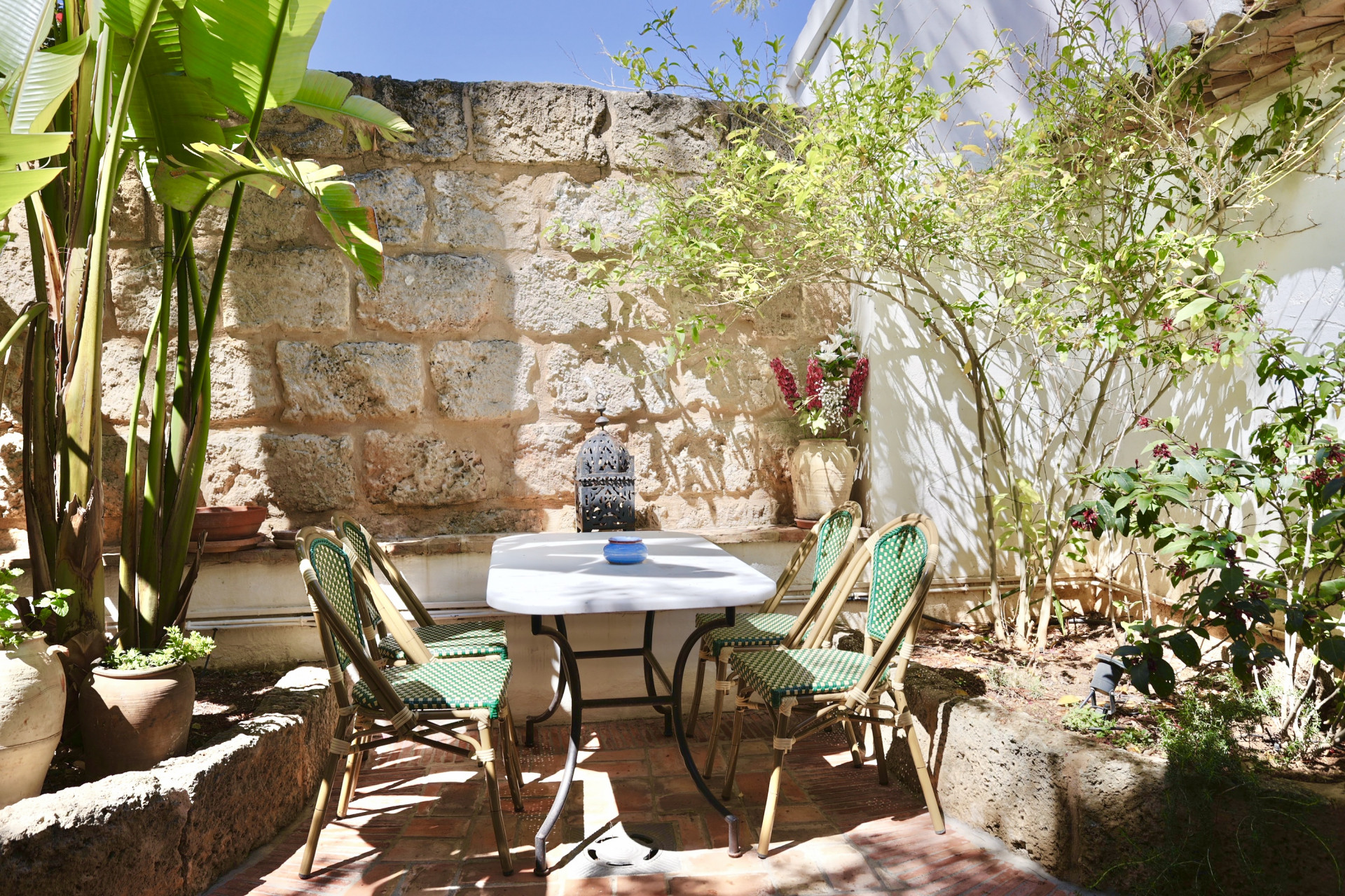 Patio mit Marmortisch, Korbstühlen und rustikaler Steinmauer. Ruhiges, natürliches Ambiente.